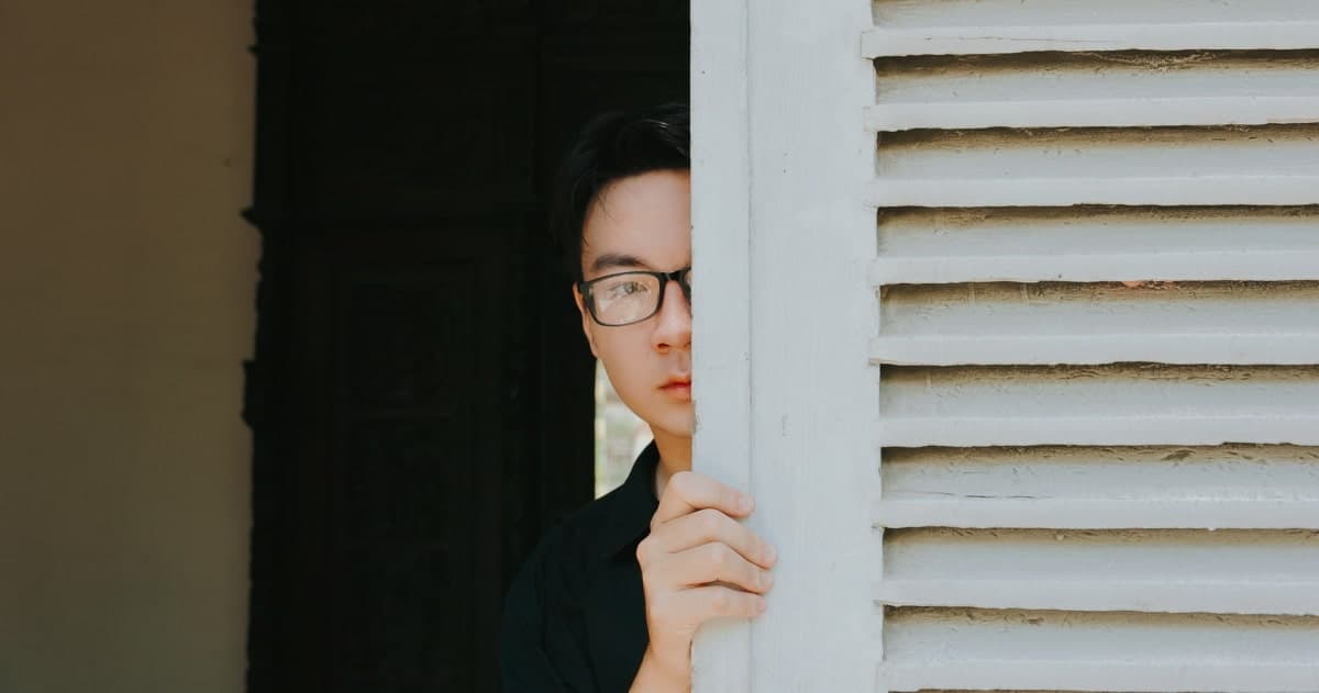 person sneaking behind white louvered wall peeking